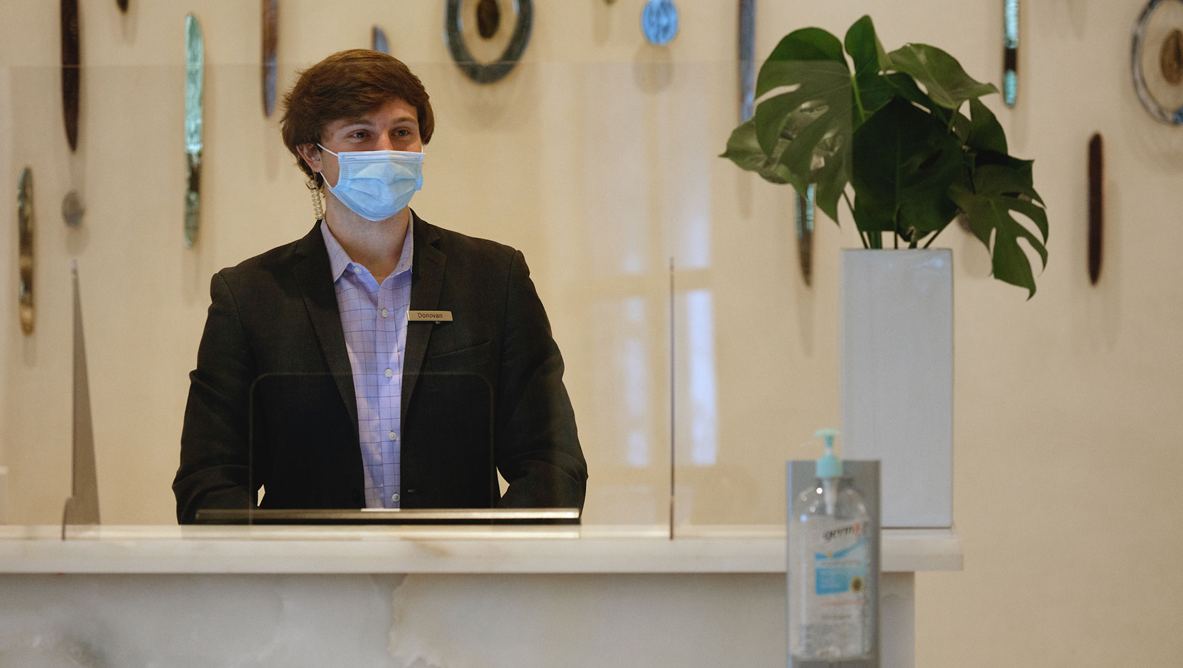 desk clerk with mask on in socially distant lobby